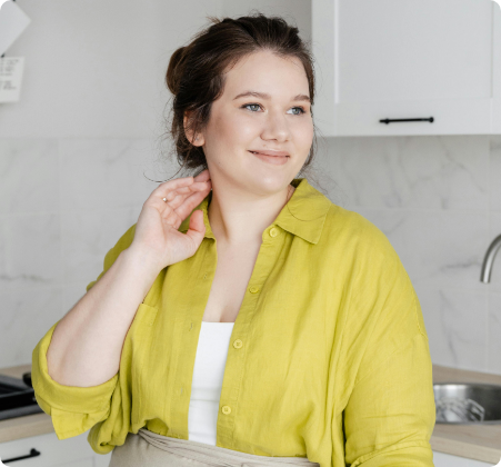 Woman in a yellow shirt smiling in a kitchen, her hand touching her hair, with a marble background and weight management book.