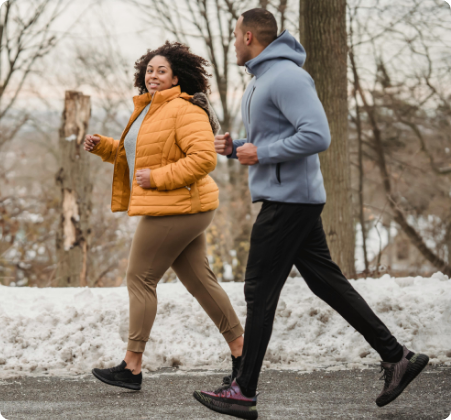 Two people managing their weight by jogging together on a snowy path, one in a yellow jacket and the other in a gray hoodie.