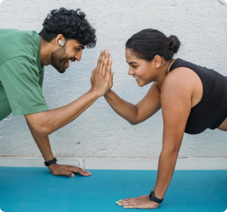 Two people doing a partner yoga pose on a blue mat, smiling and touching hands in a high-five gesture against a light blue wall, as part of their weight management routine.