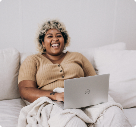 Woman sitting on a couch and laughing while using a Dell laptop to research weight management strategies.